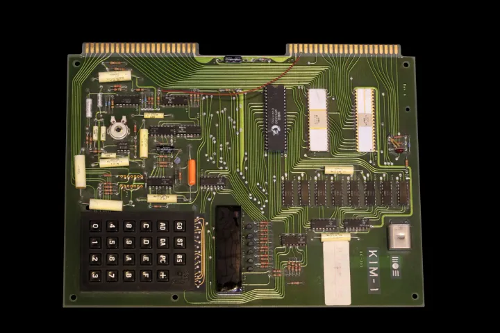 The same KIM-1 board photographed from above its other end on black, so the keypad is at the bottom left, the edge connector along the top and the KIM-1 name at the bottom right, with a loose red wire running across the left of the board.