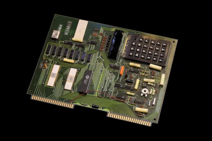 The same KIM-1 board photographed at a low angle from one corner, so that the heights of its parts show: the keypad's raised bezel, the display window, the crystal's can, the chips and the cream capacitors standing on the green board.