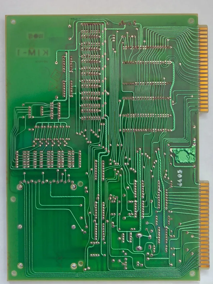 The solder side of the same Rev B KIM-1, seen from directly above on white: green lacquer over tinned tracks, rows of solder joints where the chips' legs come through, and the gold edge contacts now on the right.