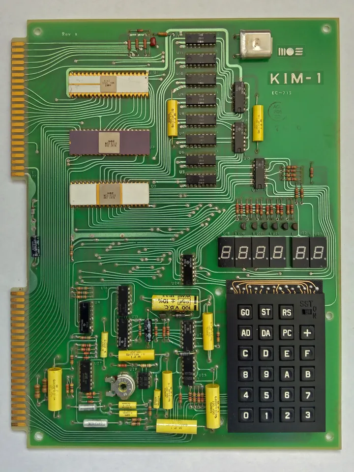 Another original KIM-1 of the same revision, seen from directly above on white: a bright green board with yellow capacitors, two white ceramic chips and a purple one, the six separate LED digits and the black keypad.